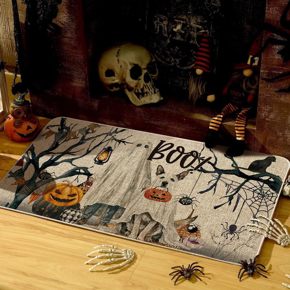 A rectangular Halloween-themed rug with a spooky woodland design, placed on a wooden floor in a decorated room. The rug features the word 'BOOY' in large script, along with pumpkins, cobwebs, spiders, bats, and a haunted house motif.
