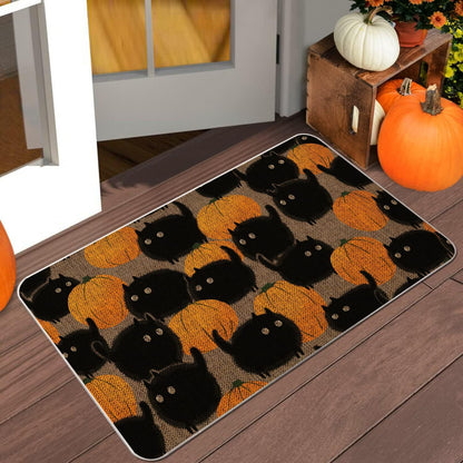 A rectangular doormat with a black cat and orange pumpkin pattern, shown on a wooden porch next to pumpkins and a crate.