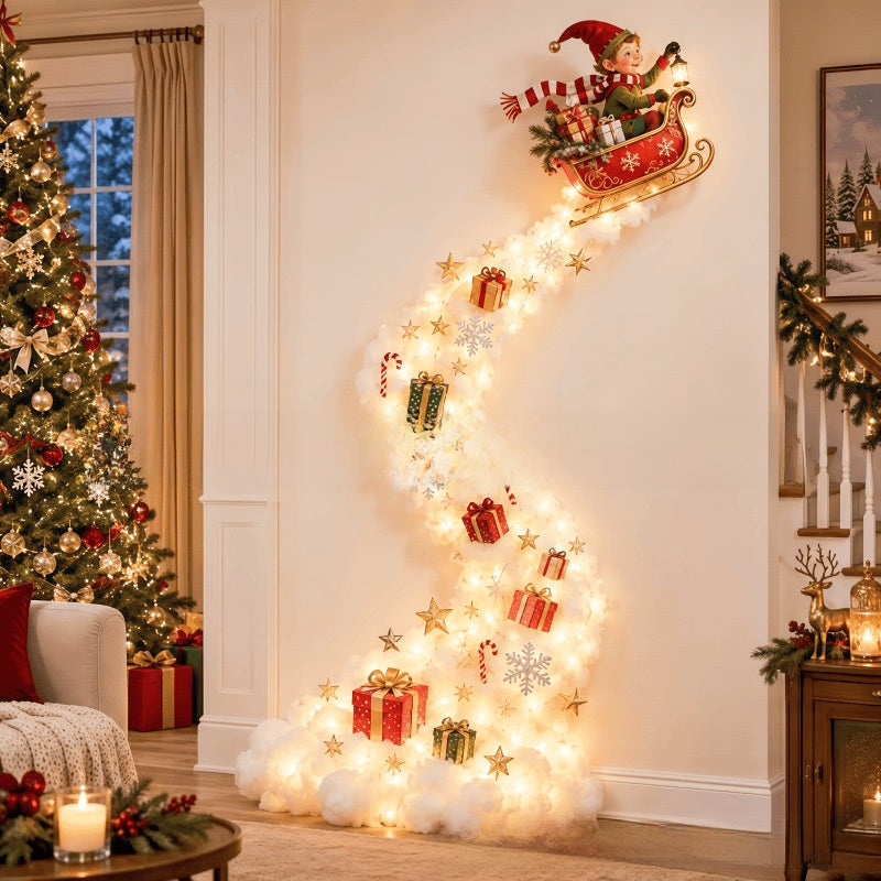 A festive Christmas wall decoration featuring a glowing light trail shaped like a staircase, with Santa in a sleigh at the top, gold stars, candy canes, snowflakes, and wrapped gift boxes, displayed in a decorated living room next to a Christmas tree.