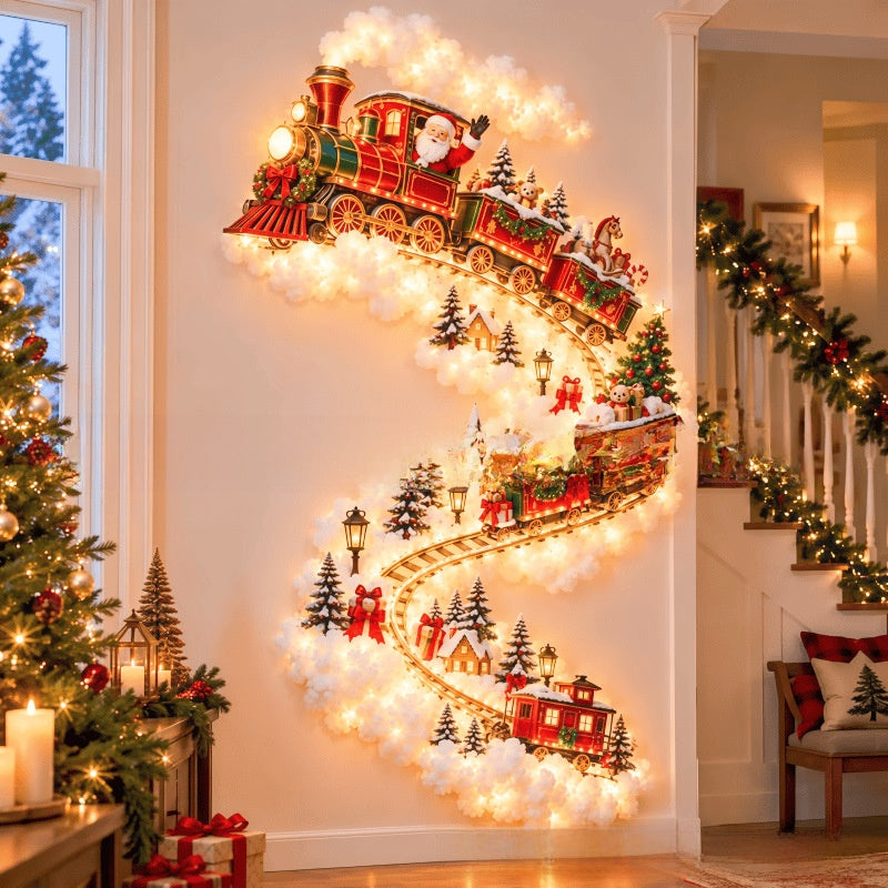A large Christmas wall mural featuring a red and green steam train traveling along tracks surrounded by fluffy white clouds, small evergreen trees, and warm white string lights, displayed on a wall in a decorated holiday living room.