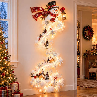 A decorative Christmas snowman wall hanging with a red scarf, black top hat, lantern, and glowing white lights, displayed on a wall in a decorated holiday home next to a lit Christmas tree.