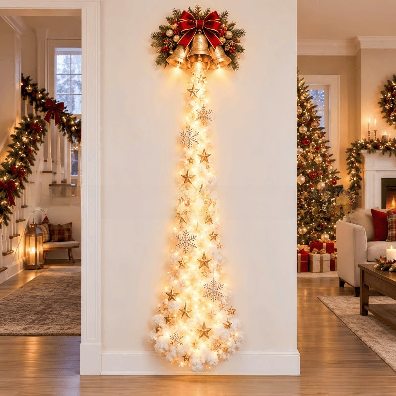 A vertical Christmas tree decoration shaped like a taper with warm white lights, gold stars, white snowflakes, and a red bow with green garland at the top, displayed in a decorated living room.