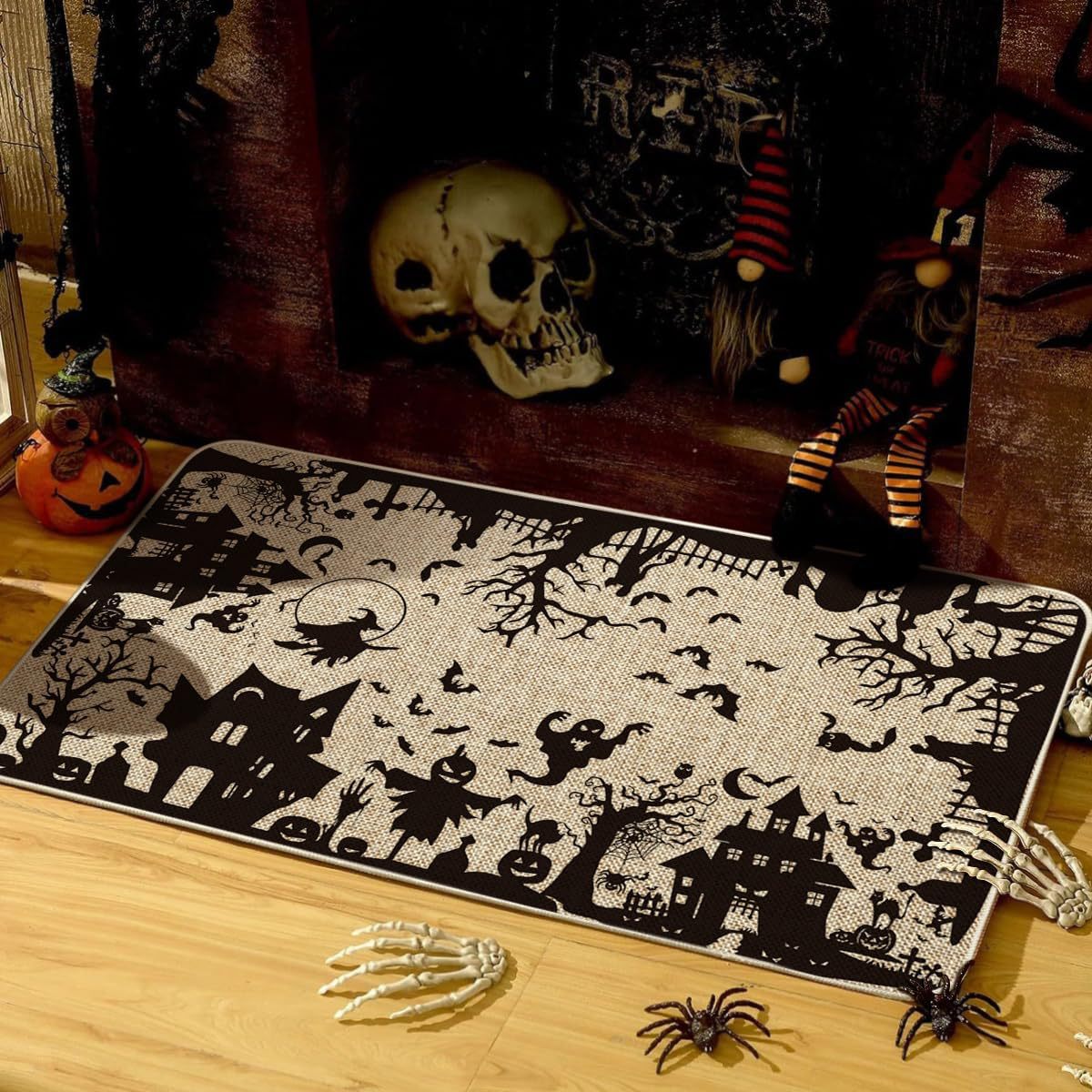 A rectangular Halloween-themed rug with a black and off-white spooky print featuring haunted houses, bats, trees, and a full moon, styled on a wooden floor with seasonal props including a skull, gnomes, spiders, and skeleton hands.