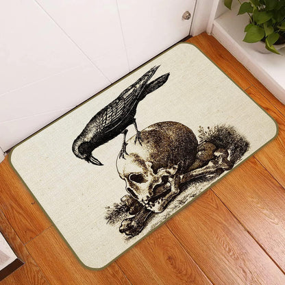 A rectangular doormat with a gothic design featuring a black raven perched on a skull and crossbones, displayed on a wooden floor in front of a white door.