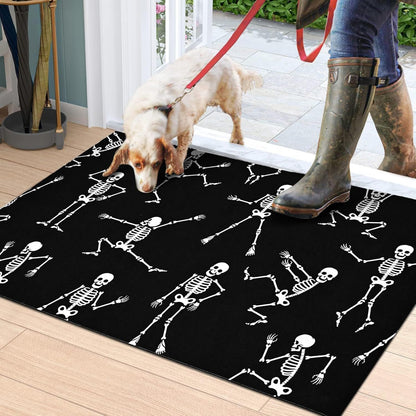A black rectangular doormat with a white skeleton pattern, shown on a wooden porch floor. A dog is standing on the mat, and a person wearing green rubber boots and a red leash is also visible.