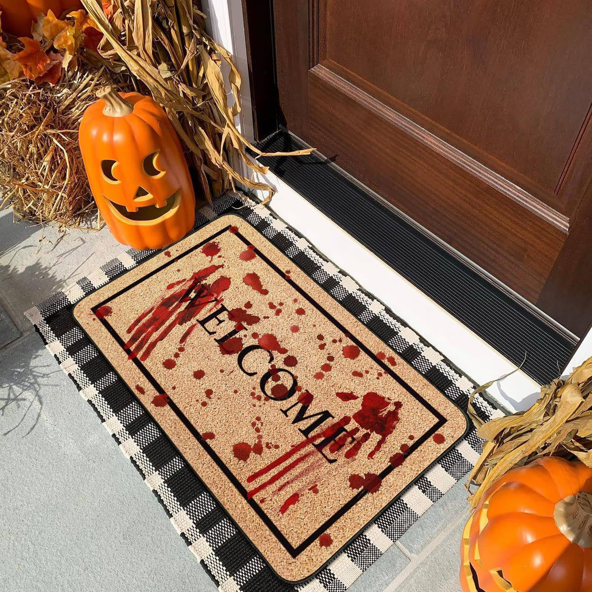 A Halloween-themed welcome doormat with a blood splatter design and the word 'WELCOME' in black, placed on a front porch next to a jack-o'-lantern and fall decorations.