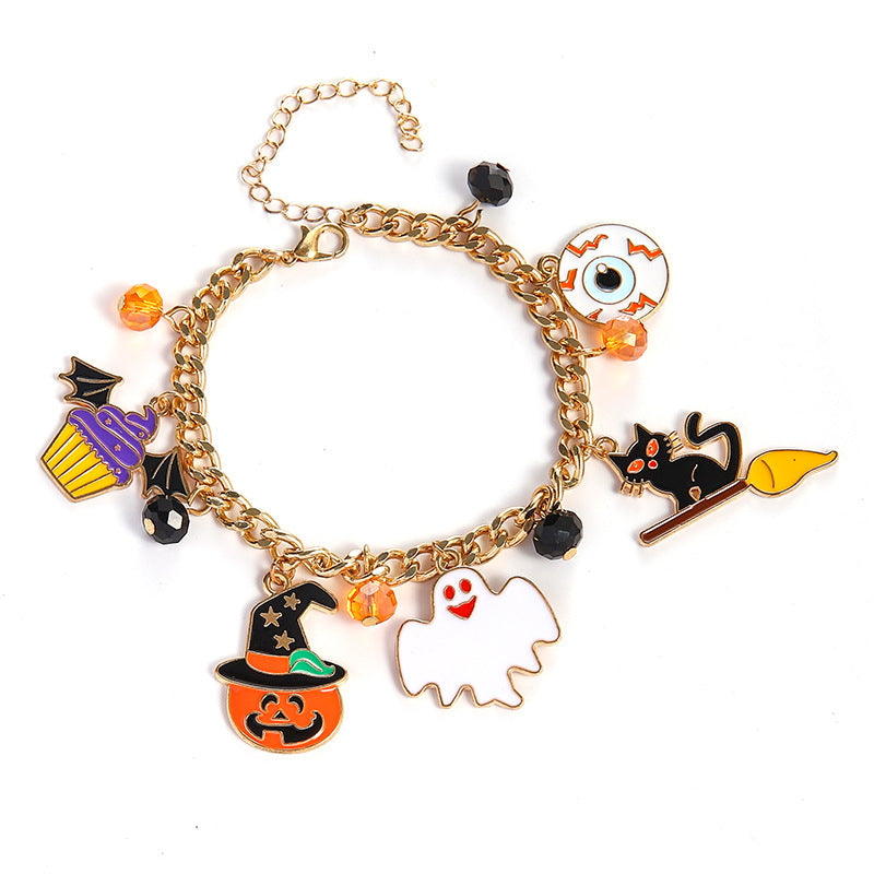 A gold-tone chain charm bracelet featuring Halloween-themed enamel charms including a witch hat pumpkin, ghost, black cat on a broomstick, eyeball, cupcake, bats, and orange beads, displayed on a clean white background.