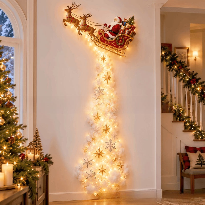 A festive Christmas wall decoration featuring Santa Claus in a sleigh pulled by reindeer, with a glowing vertical tree of white lights and gold star ornaments hanging on a white wall in a decorated home interior.