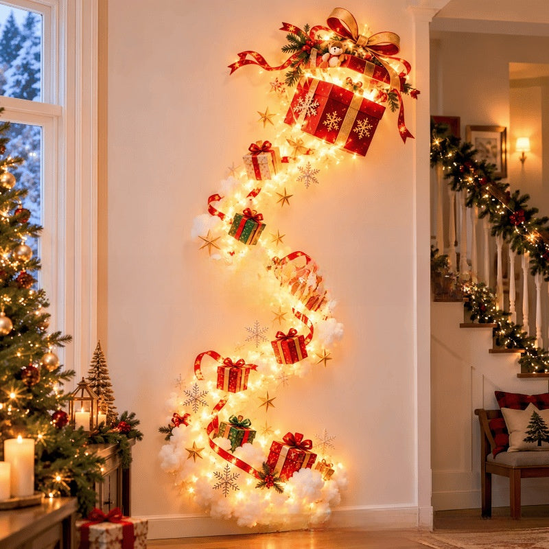 A festive spiral Christmas wall decoration featuring glowing warm white fairy lights, red gift boxes with gold snowflake patterns, white fluffy cloud accents, and green pine garlands, displayed on a wall in a decorated holiday home interior.