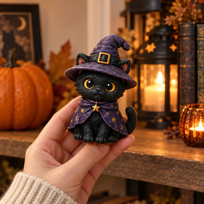 A small black cat figurine dressed as a witch, held in a person's hand against a warm, cozy autumn background with a pumpkin, lantern, and candles.